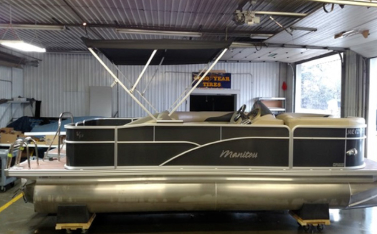 Fully repaired black Manitou pontoon boat with crisp side paneling and raised bimini top.