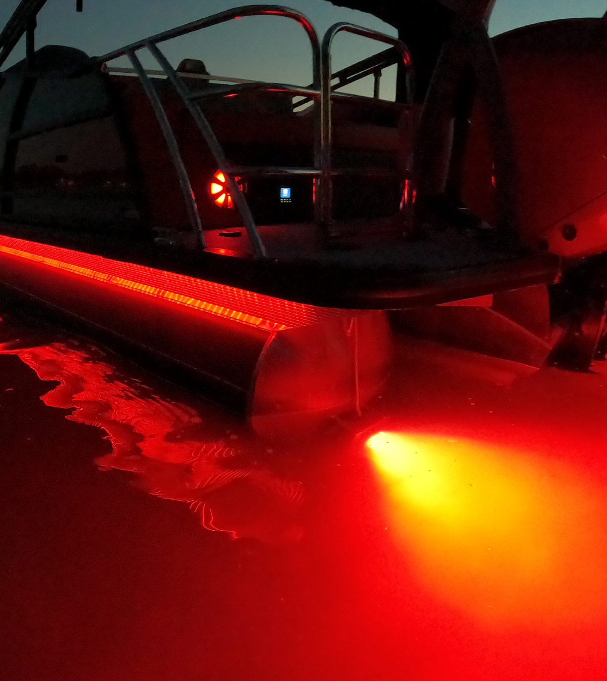 Pontoon boat deck at night illuminated by red LED strip lighting along the pontoon tube and underwater LED lights.