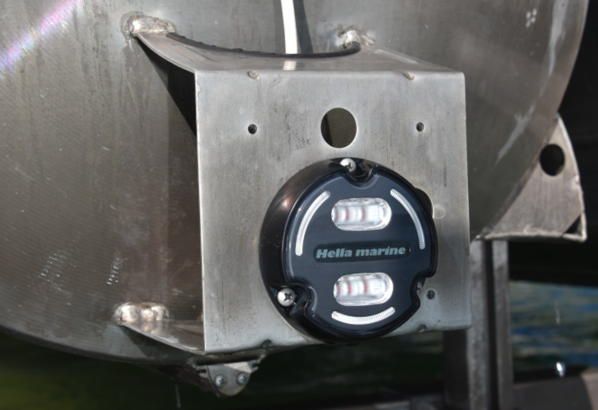 Close-up of a black Hella marine LED light fixture mounted to a metal bracket on a pontoon log.