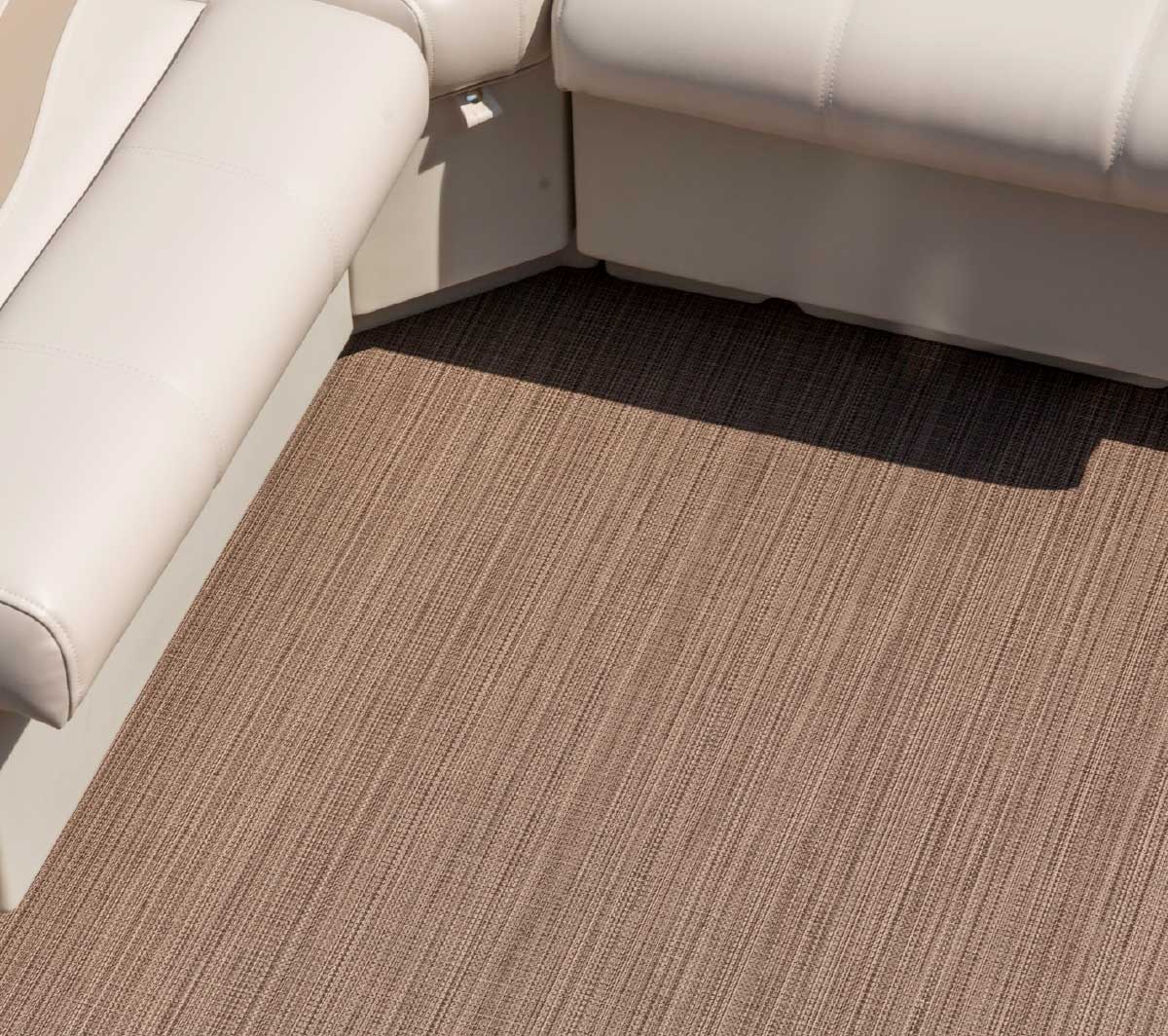 High-angle view of textured tan marine carpet flooring installed in a pontoon boat next to beige vinyl seating.