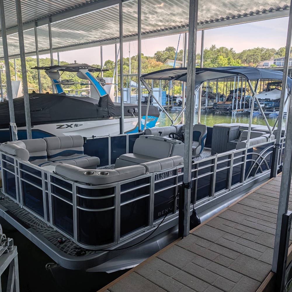 A clean, refurbished pontoon boat with blue trim parked under a covered marina boat slip