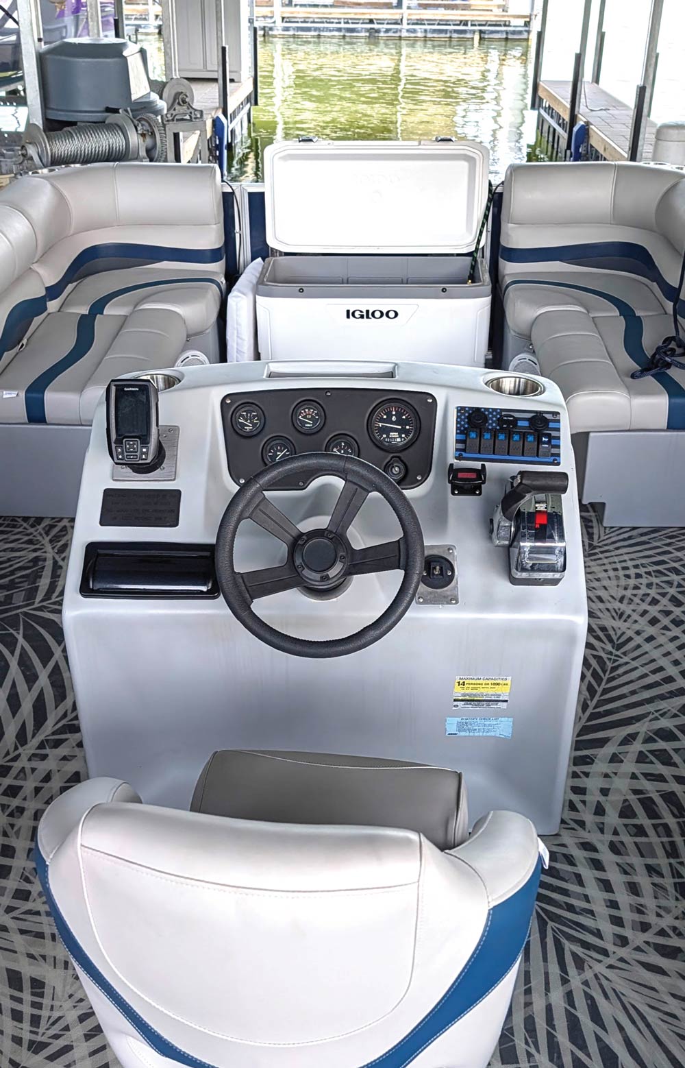View from behind the captain's chair showing the steering console and Igloo cooler on a pontoon boat.