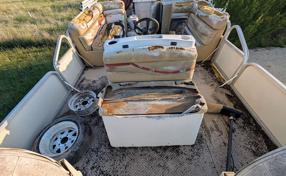 Interior view of a worn-out pontoon boat with torn upholstery, exposed foam, and spare tires on deck.