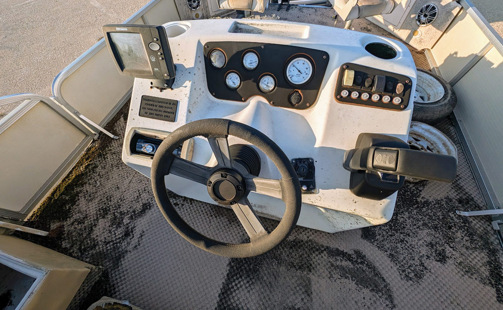 Overhead close-up of a dirty, aged white pontoon boat steering console and dashboard gauges.