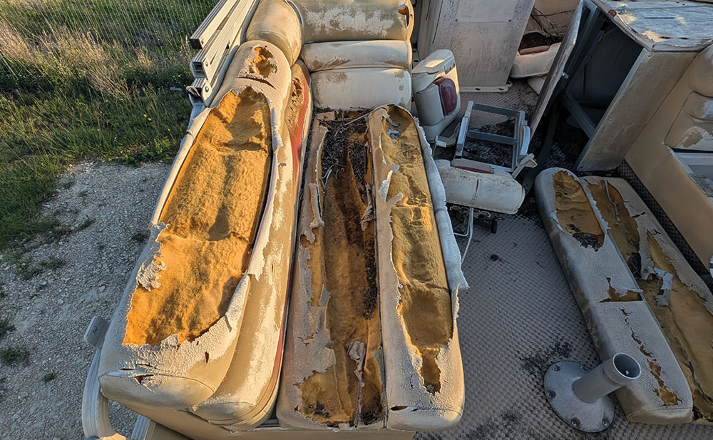 Severely damaged, torn yellow foam seats on a worn pontoon boat undergoing restoration.