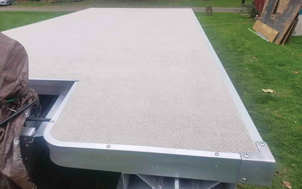 Close-up of newly installed light tan woven vinyl flooring and metal trim on a pontoon deck.