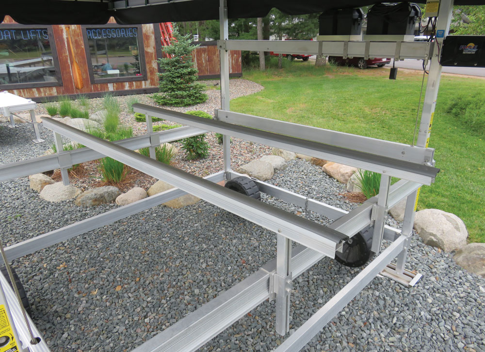 An aluminum boat lift frame with padded bunks and wheels sitting on a gravel display area outdoor.