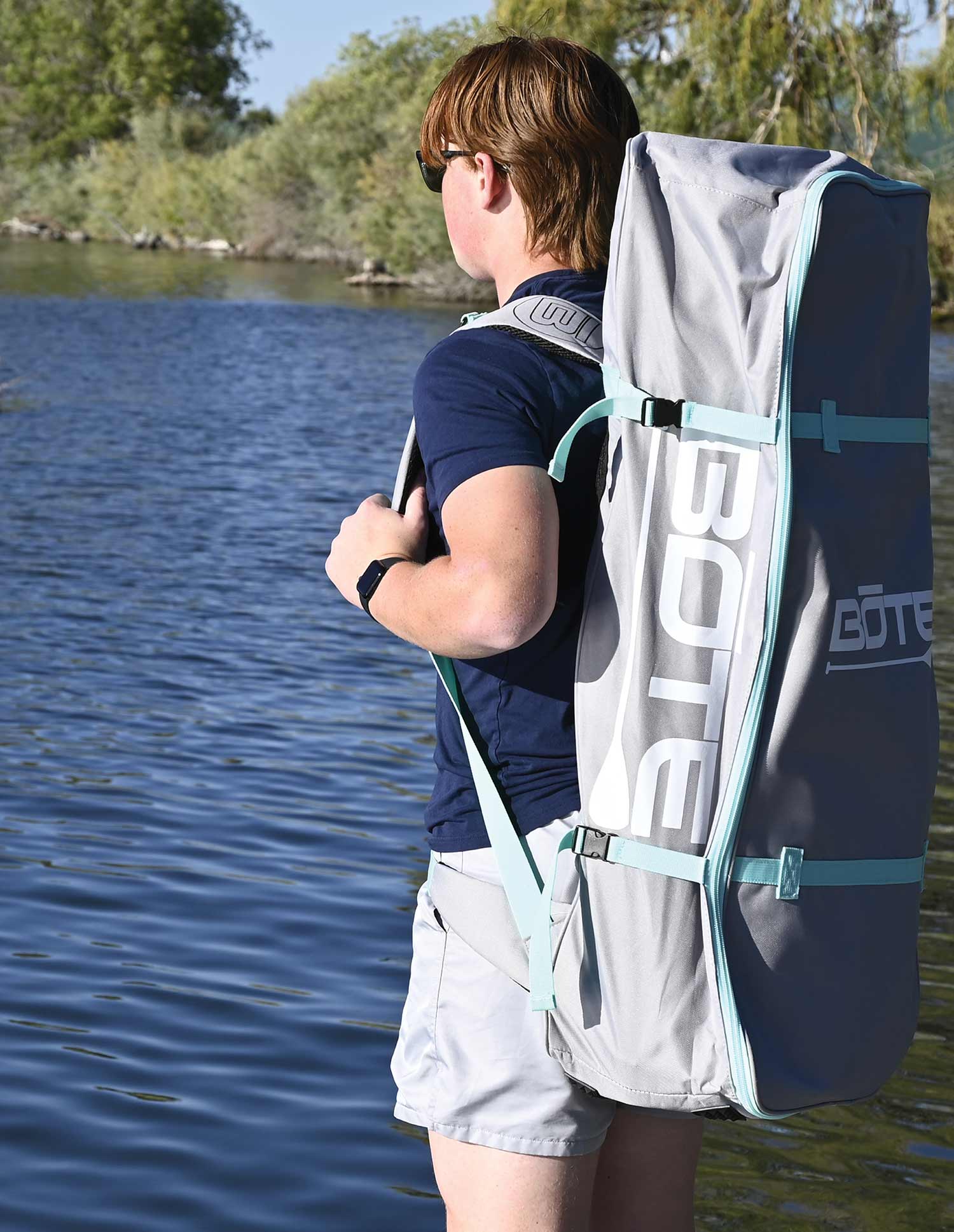 Person wearing a grey BOTE backpack carry bag near a body of water.