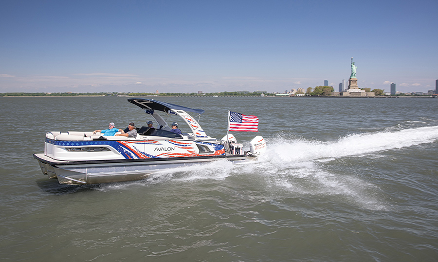 An Avalon pontoon boat with American flag graphics cruising past the Statue of Liberty.