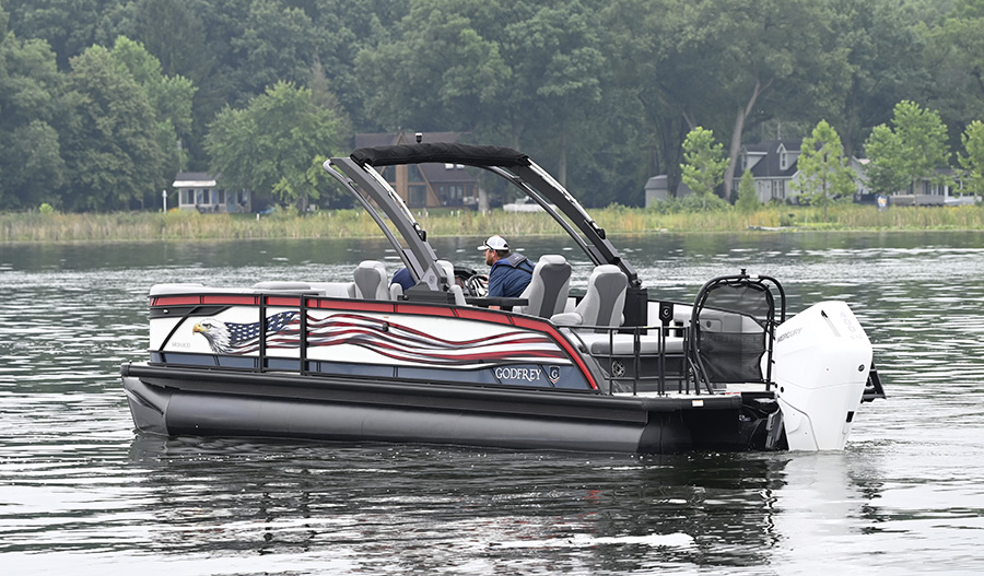 A Godfrey pontoon boat styled with bald eagle and American flag graphics navigating calm waters.