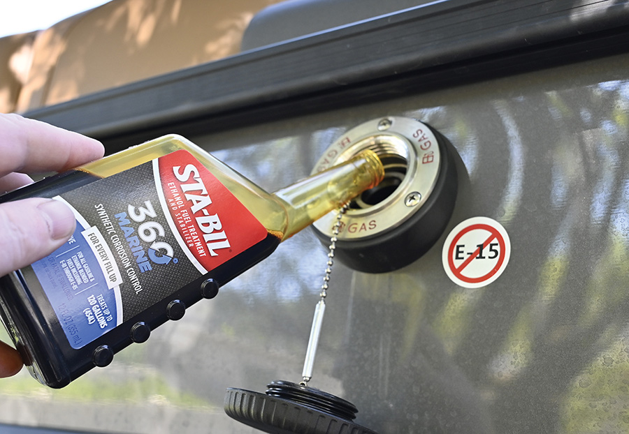 A person pouring marine fuel stabilizer into a boat's gas tank opening.