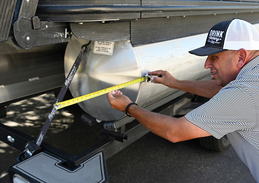 A man using a tape measure to check the diameter of a pontoon boat tube.