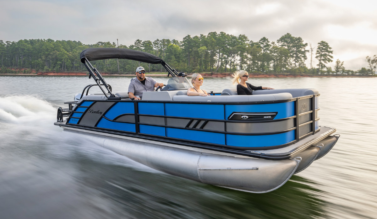 Blue and black Bentley pontoon boat cruising across a lake with passengers aboard.