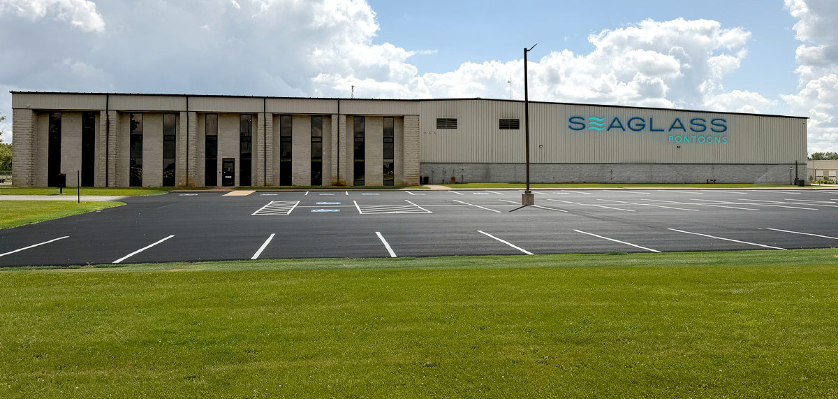 Large white industrial facility and parking lot with "SEAGLASS PONTOONS" mounted on the side.