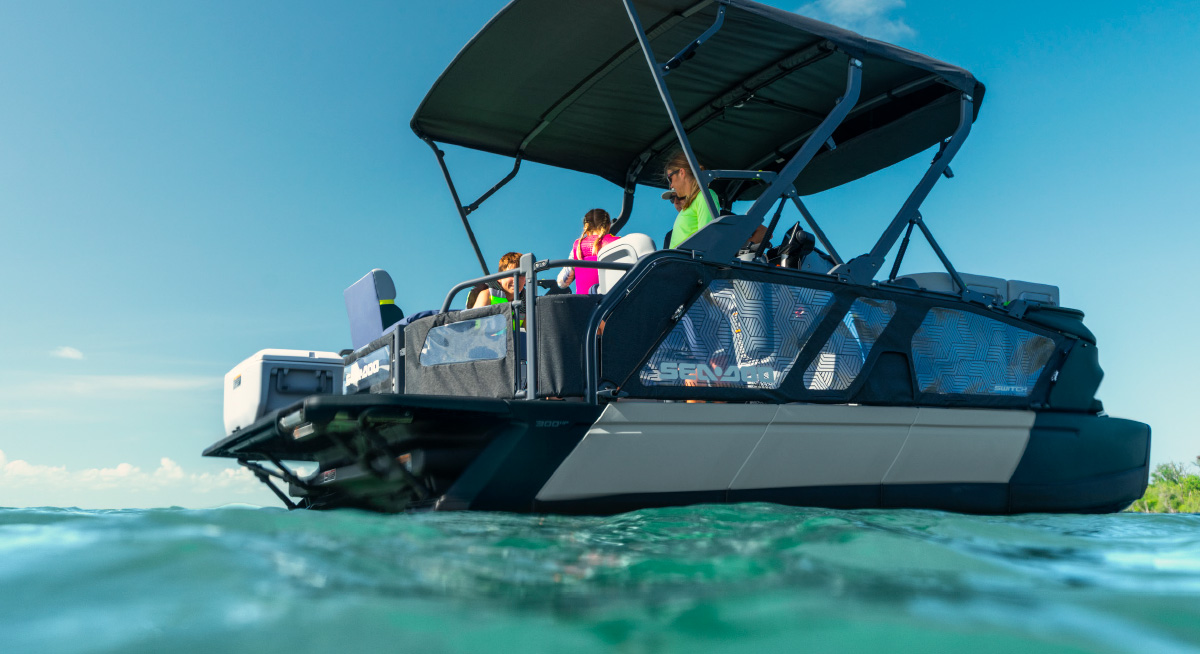 Low-angle shot of a Sea-Doo Switch pontoon boat floating on turquoise ocean water under a bimini top.