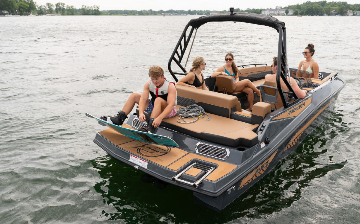 Young man securing a wakeboard binding while sitting on the swim platform of a Starcraft boat.