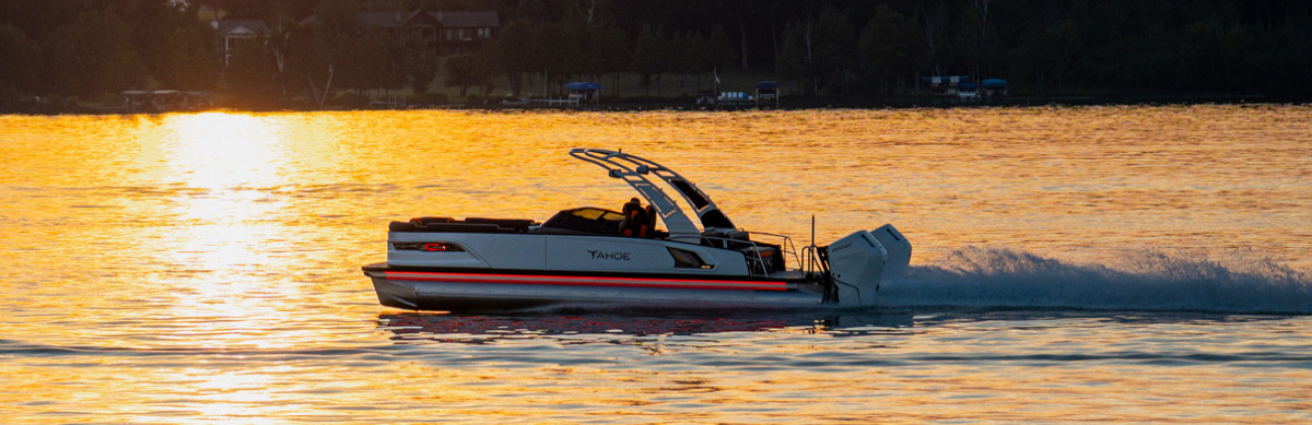 Silhouette of a Tahoe pontoon boat with red accent lighting speeding across water at golden hour.