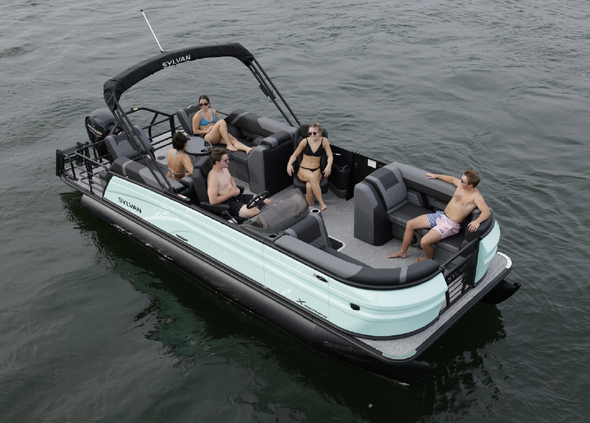 High-angle view of a light blue Sylvan pontoon boat carrying five passengers across calm water.