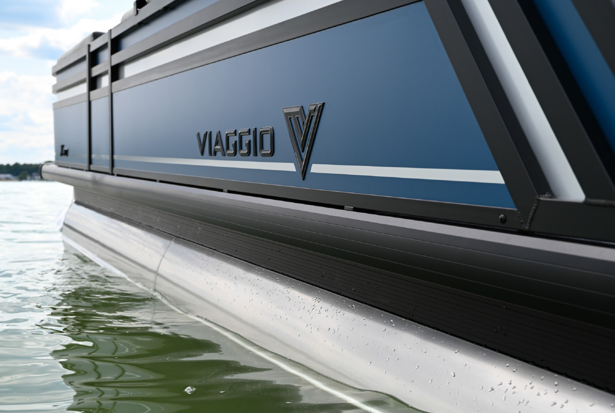 Close-up view of the metallic blue hull and "VIAGGIO V" logo of a pontoon boat resting on water.