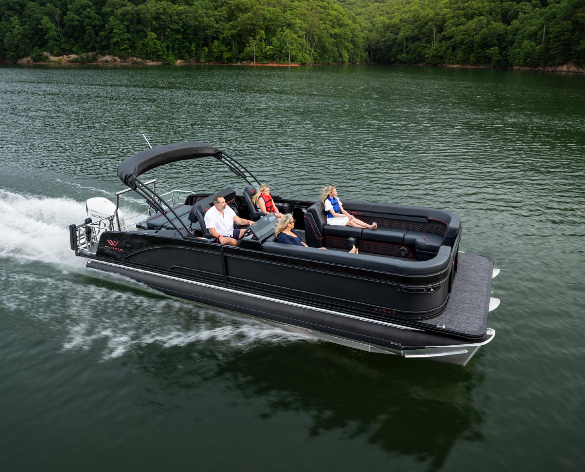 High-angle shot of a sleek black Whisper Cloud pontoon boat carrying four passengers across a calm lake.