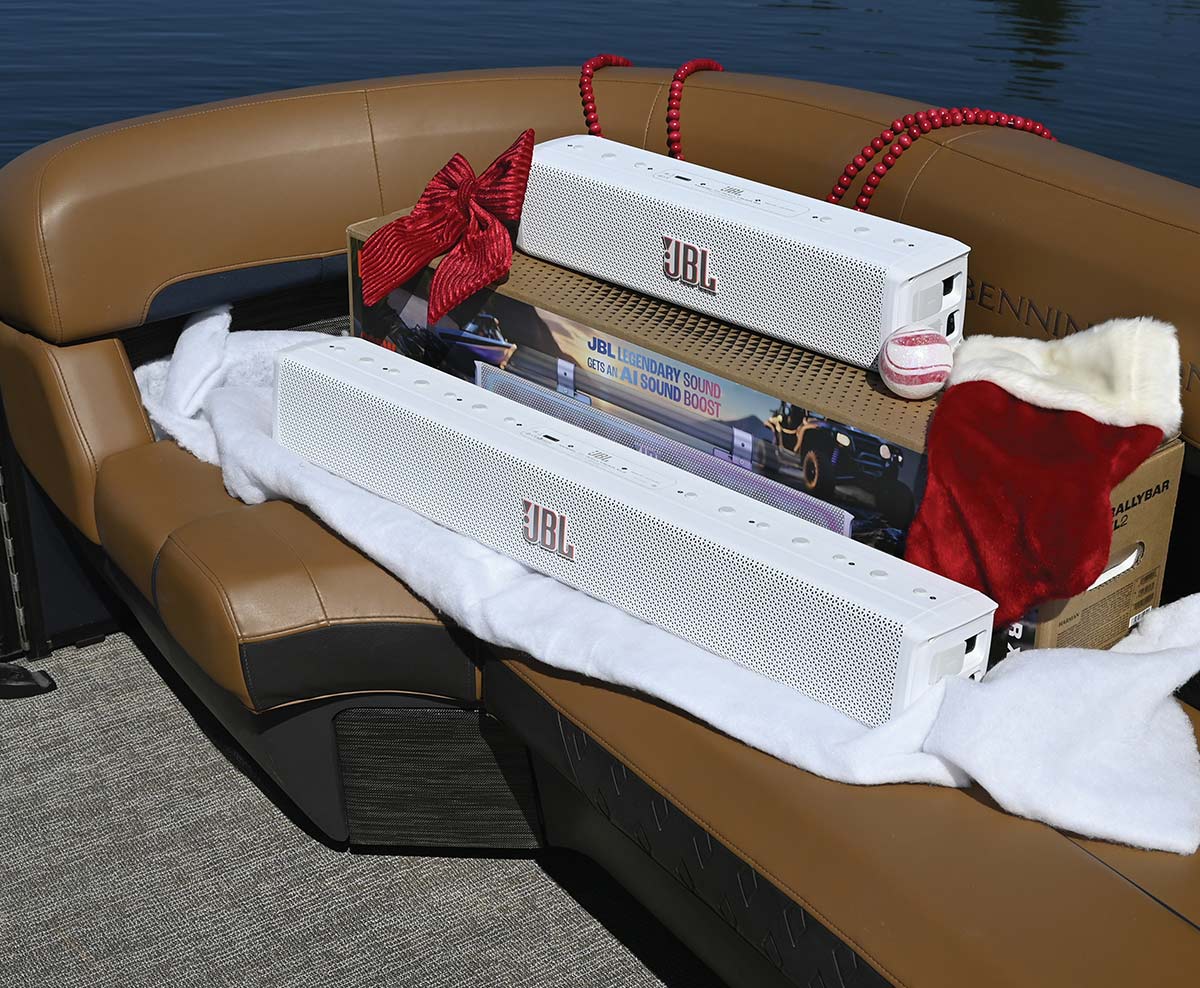 Two white JBL soundbars displayed on a brown leather pontoon boat seat alongside festive holiday decorations and product packaging.