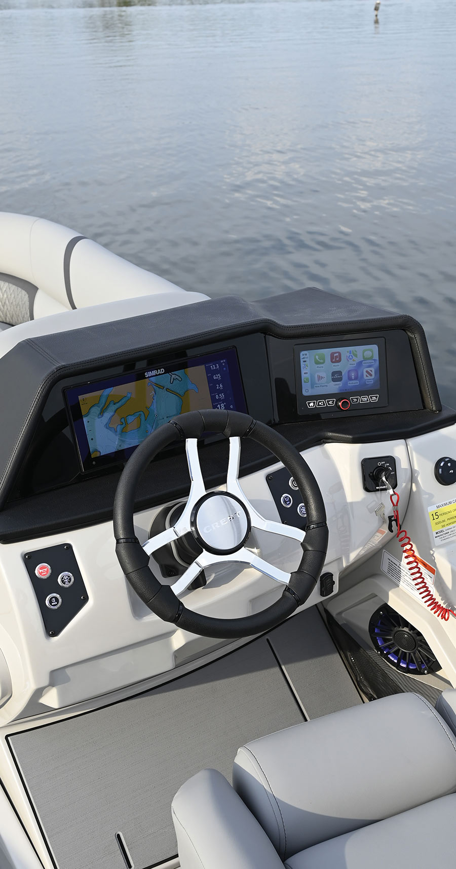 The helm console of a Crest pontoon boat featuring a steering wheel and digital Simrad navigation displays.   